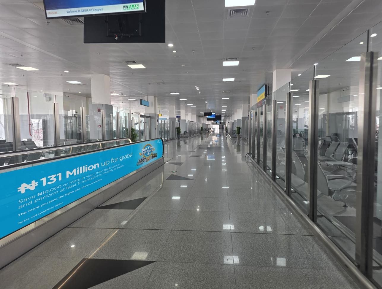 ABV-064 · Glass and Travelator Branding — Nnamdi Azikiwe International Airport, Arrival Corridor advertising face and surrounding environment